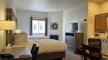 A hotel room with a bed, desk, chair, TV, microwave, and a small kitchenette.