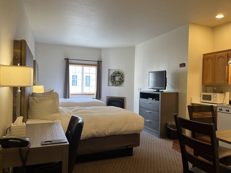 A hotel room with a bed, desk, chair, TV, microwave, and a small kitchenette.