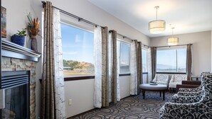 A room with a fireplace, large windows with curtains, a patterned carpet, and a seating area with a table and chairs. - Sunrise Inn Villas and Suites (Anacortes)