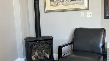 A room with a black leather chair, a black wood-burning stove, and a framed cityscape painting on the wall.