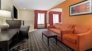 A hotel room with a sofa, a table, a TV, and a window with curtains. - Best Western Kenosha Inn (Broken Arrow)