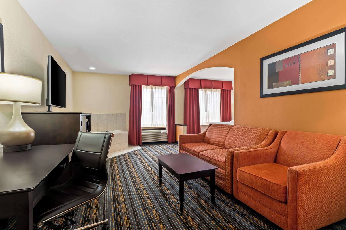 A hotel room with a sofa, a table, a TV, and a window with curtains.