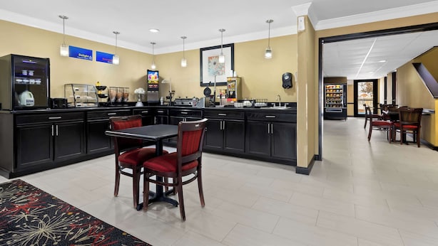 A hotel kitchen with a dining area, including a table with chairs, a coffee machine, and a refrigerator. - Best Western Kenosha Inn (Broken Arrow)