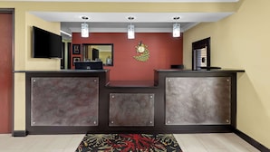 A reception desk with a flat-screen TV, a clock, and a decorative wall piece. - Best Western Kenosha Inn (Broken Arrow)