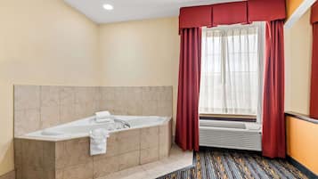 A modern bathroom with a large bathtub, a window with red curtains, and a patterned carpet.