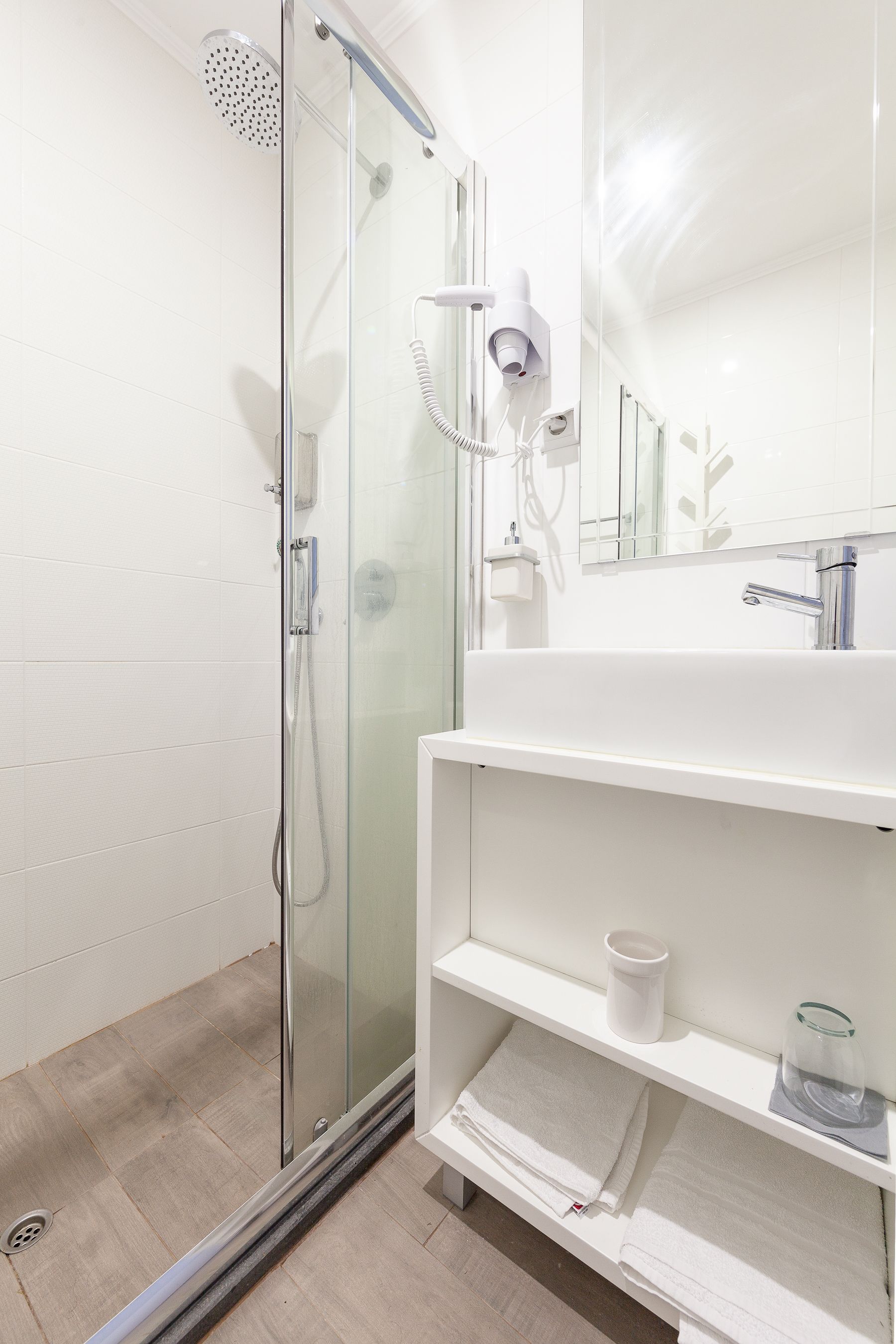 A modern bathroom with a glass shower enclosure, a white sink, and a mirror above the sink.