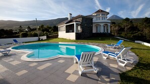 A swimming pool with lounge chairs, a stone house, and a mountain in the background. - Pico Dreams - Sportfish (Sao Roque do Pico)