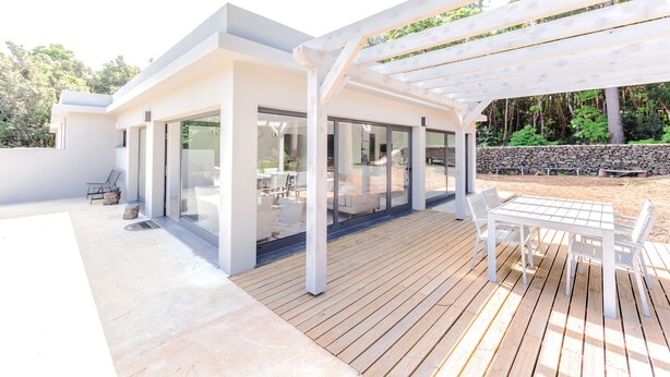 A modern outdoor patio with a wooden deck, a white pergola, and a glass-enclosed dining area. - Pico Dreams - Sportfish (Sao Roque do Pico)