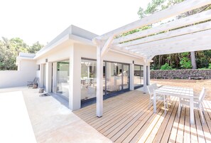 A modern outdoor patio with a wooden deck, a white pergola, and a glass-enclosed dining area. - Pico Dreams - Sportfish (Sao Roque do Pico)