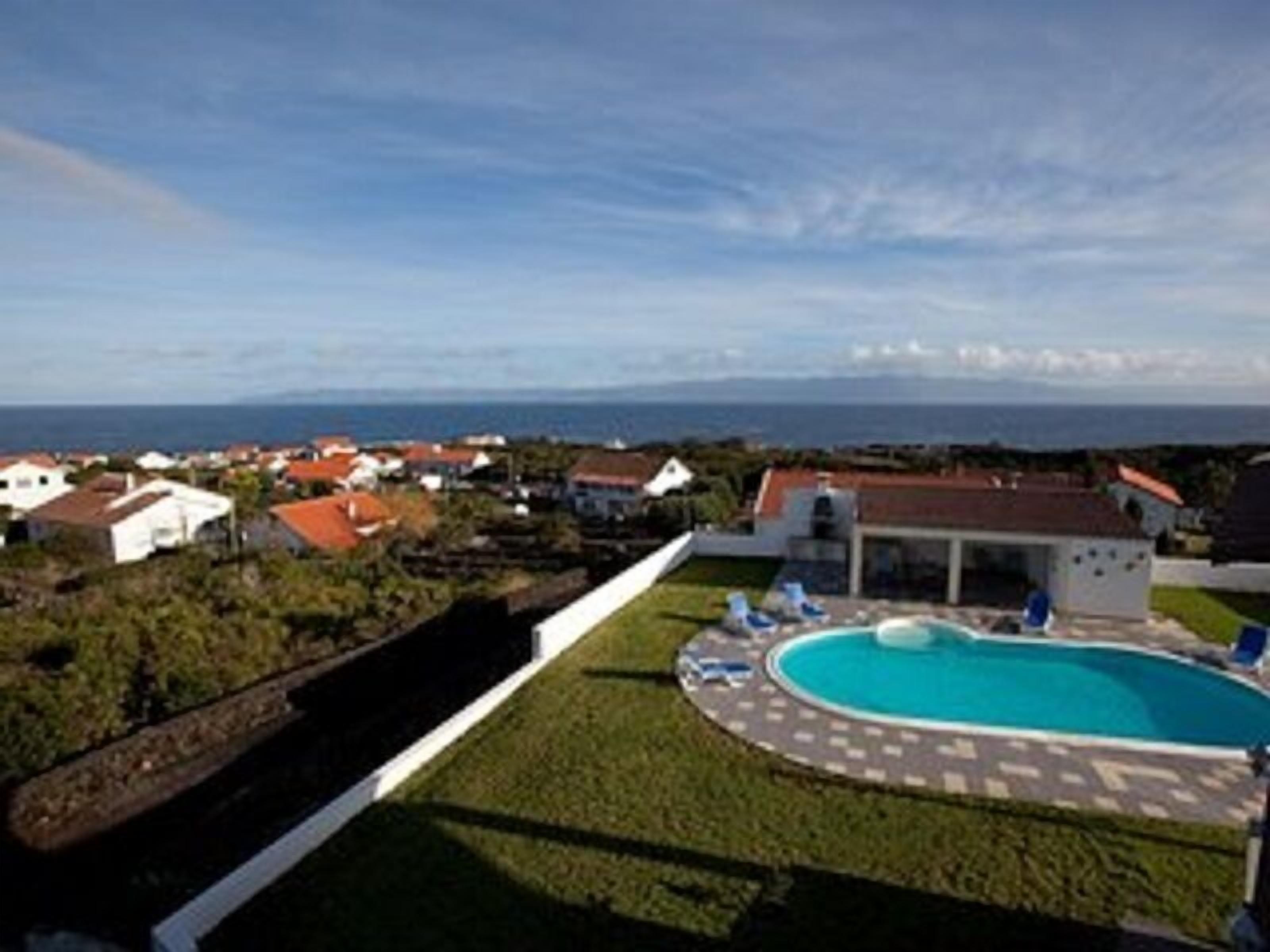 A residential area with a swimming pool surrounded by a paved deck, a small building, and houses in the background.