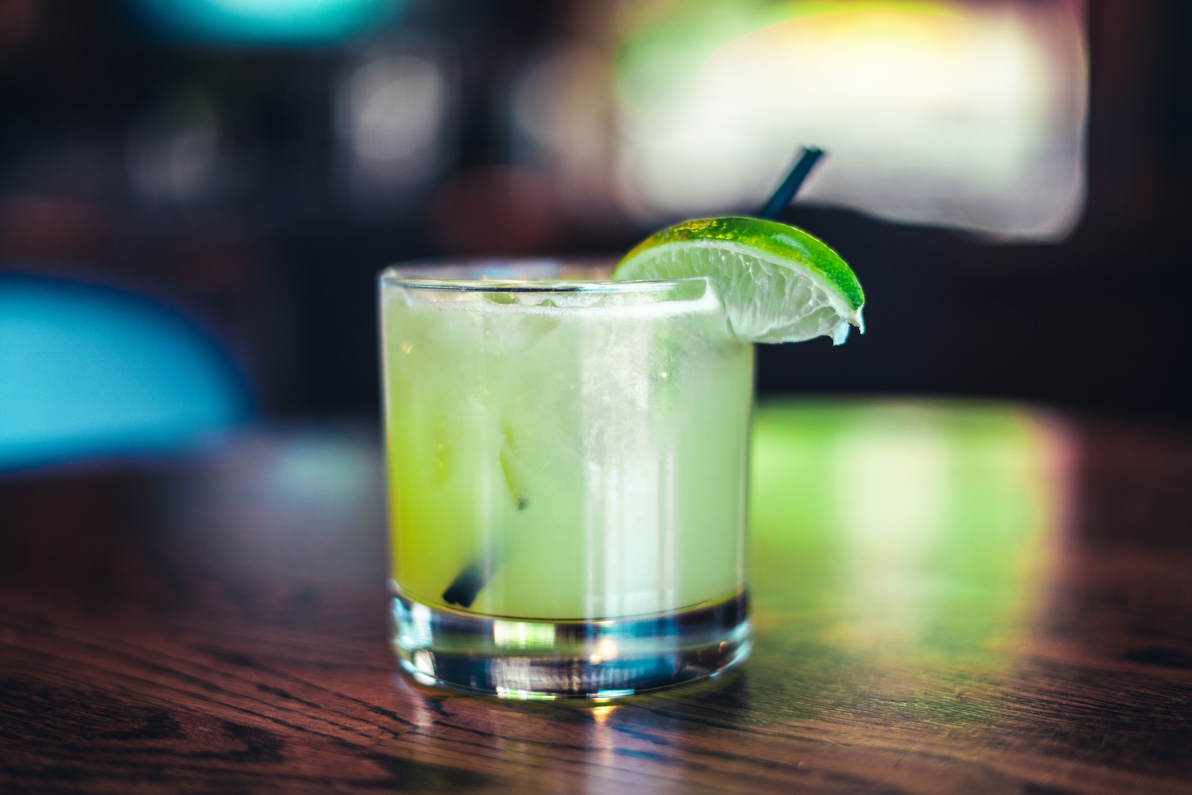 A glass of a green beverage with a lime wedge on a wooden surface.