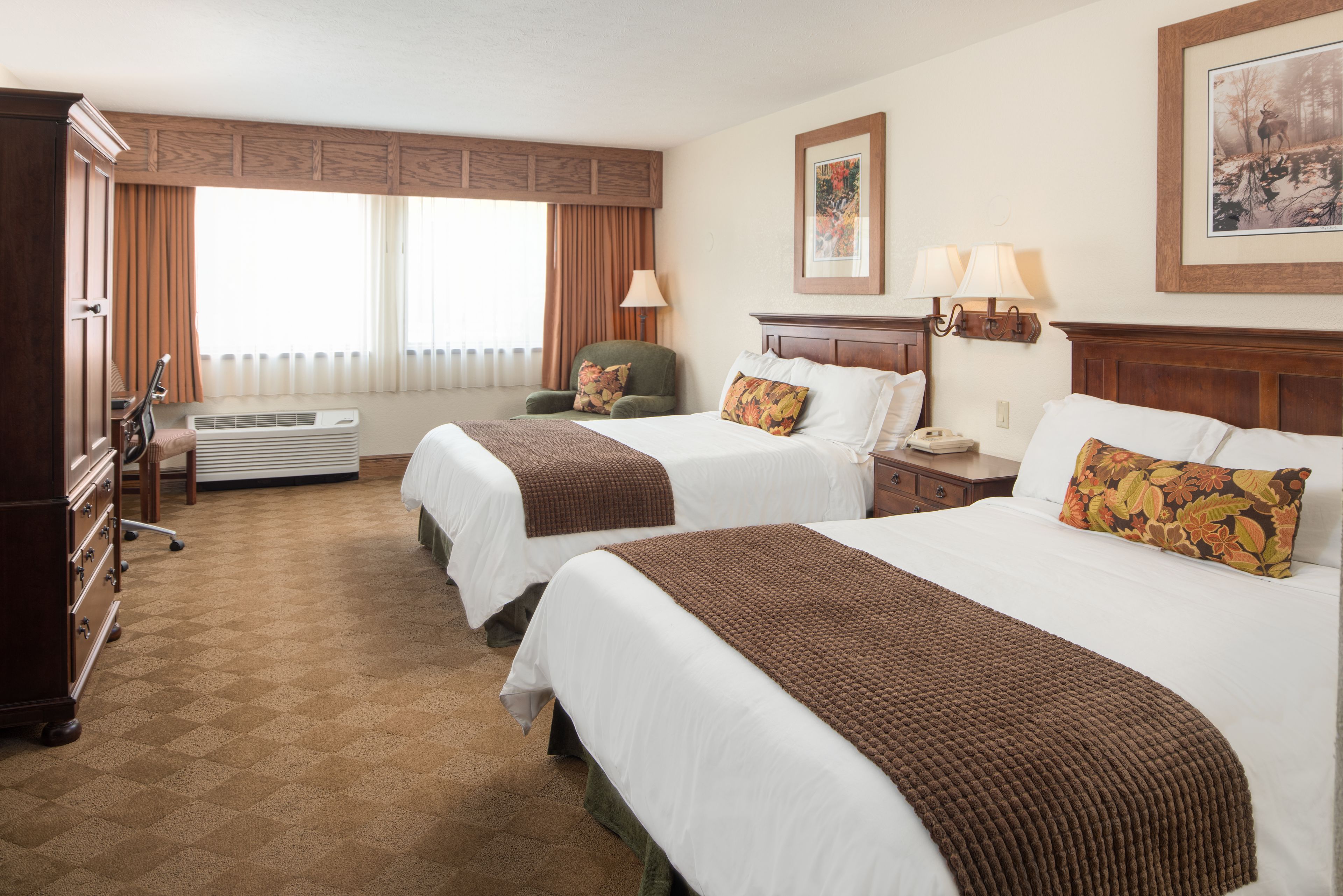 A hotel room with two beds, a dresser, a chair, a lamp, and a window with curtains.