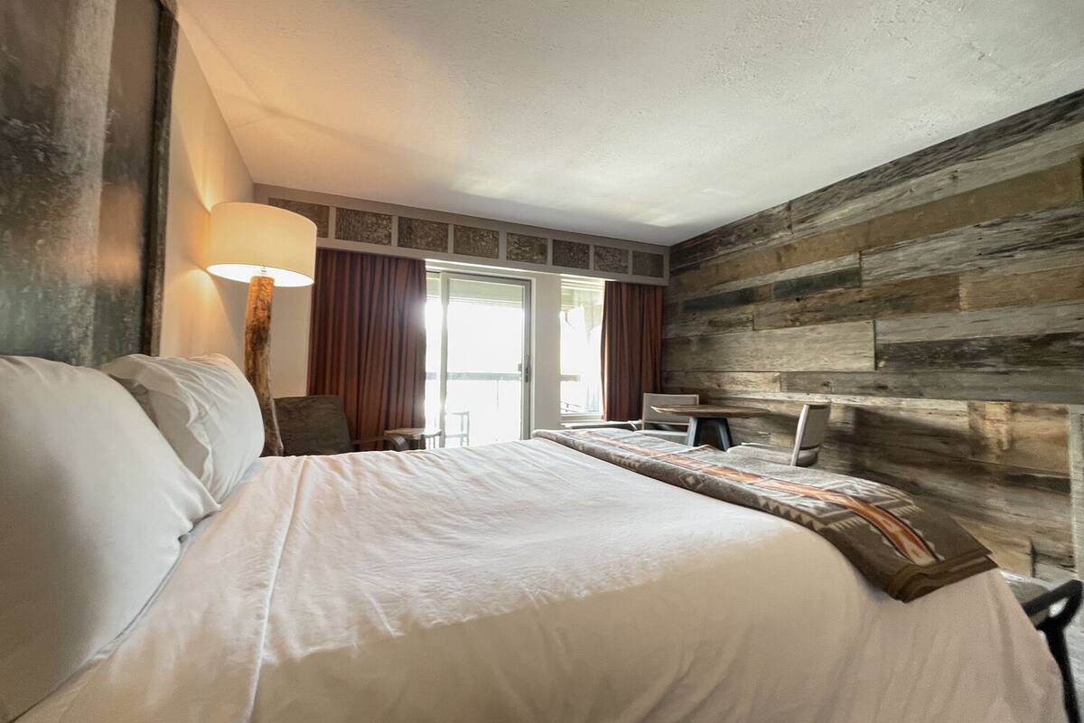 Une chambre d’hôtel avec un grand lit, un bureau et une vue sur l’extérieur grâce à une porte coulissante.