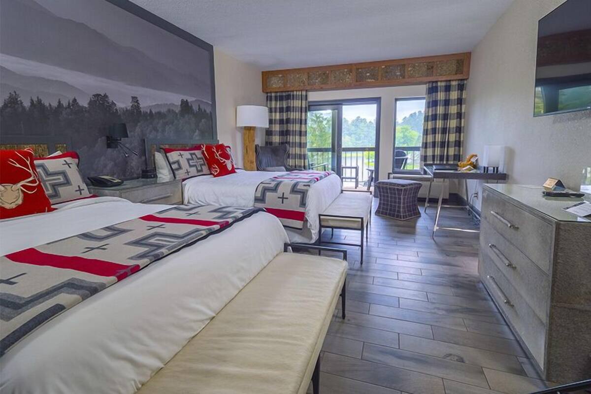 Une chambre d’hôtel avec deux lits, un bureau, une chaise, une commode et un balcon donnant sur la forêt.