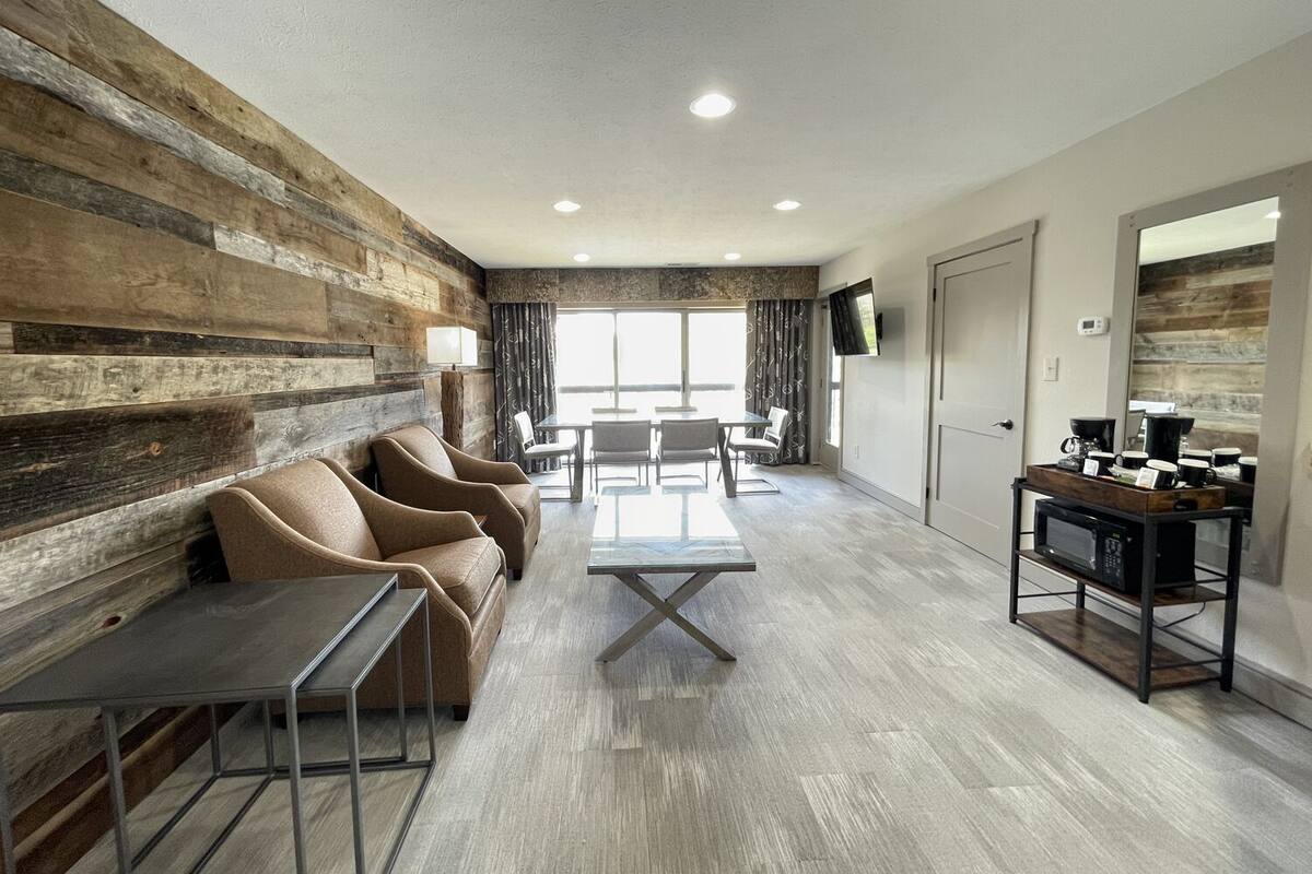 Une chambre d’hôtel moderne avec un mur d’accent en bois, un canapé, une table basse et un téléviseur fixé au mur.