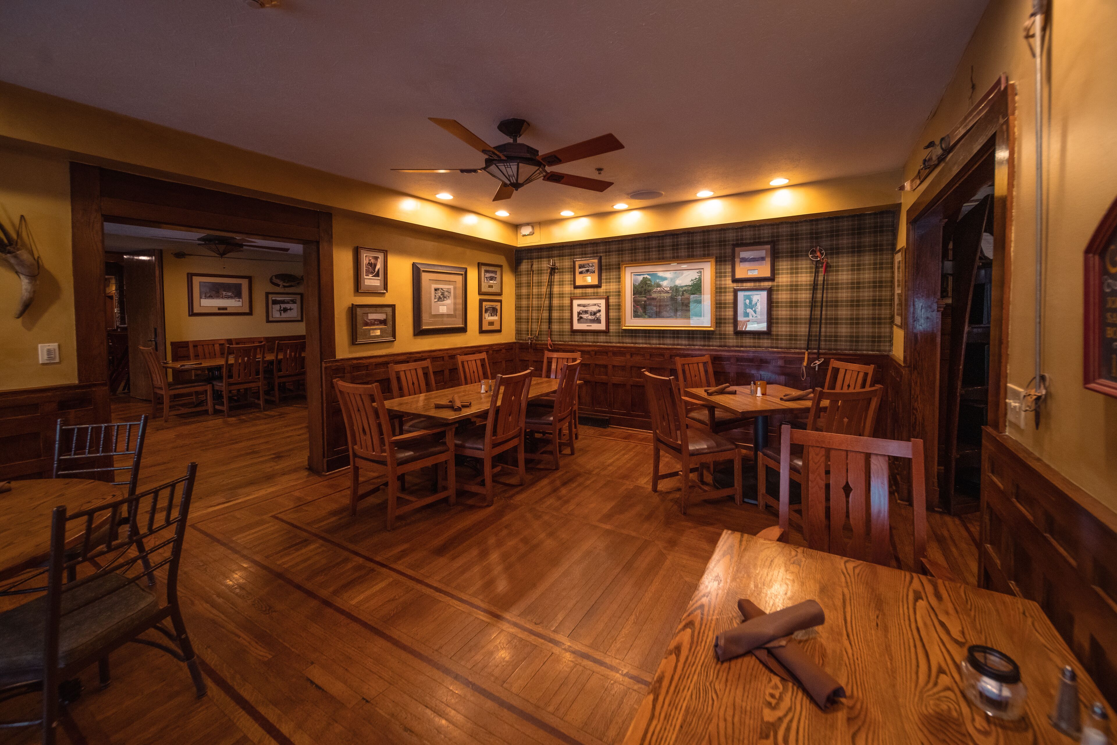 A restaurant with wooden tables and chairs, framed pictures on the walls, and a ceiling fan.