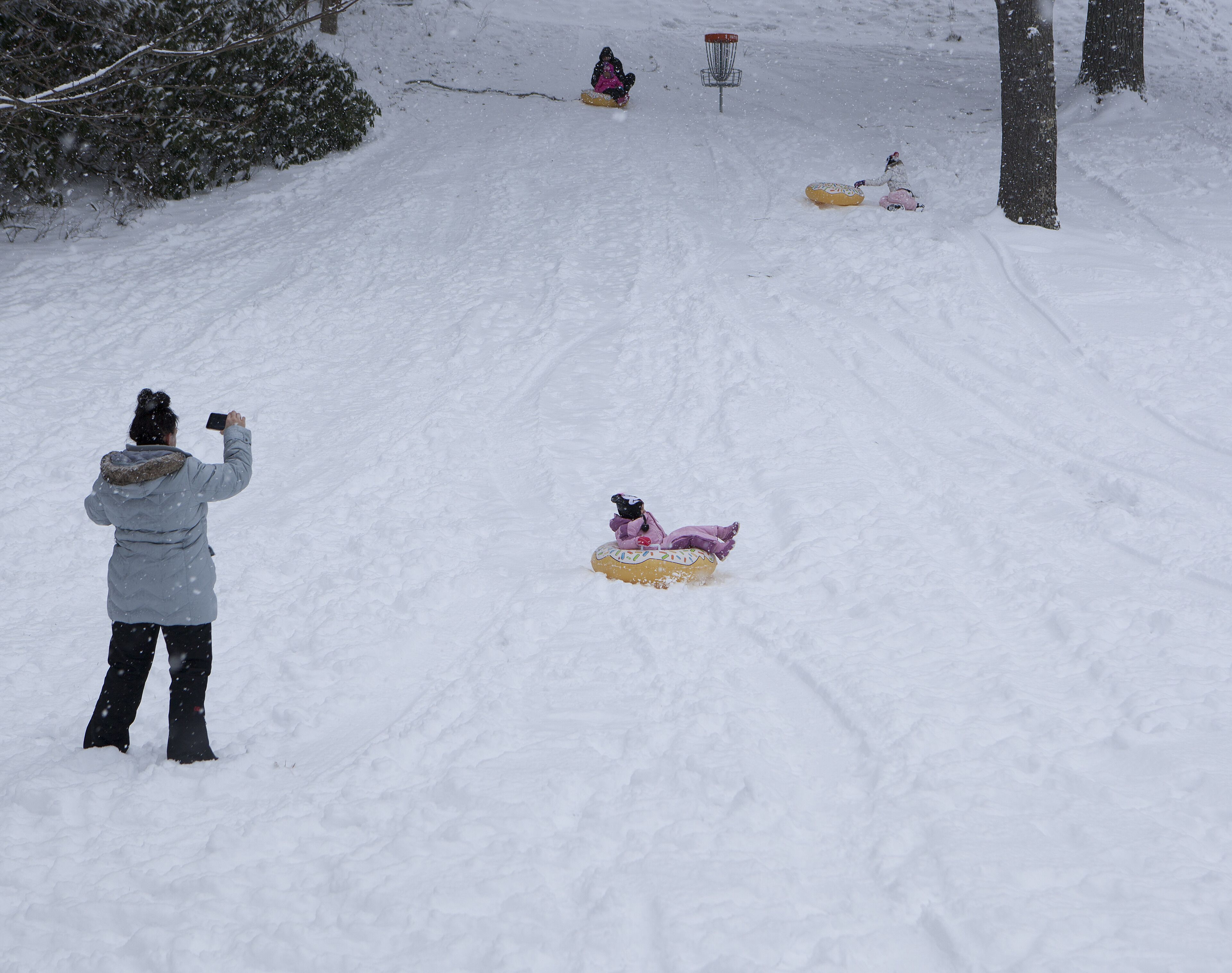 A snowy landscape with a person taking a photo, a child sledding, and a snowman.