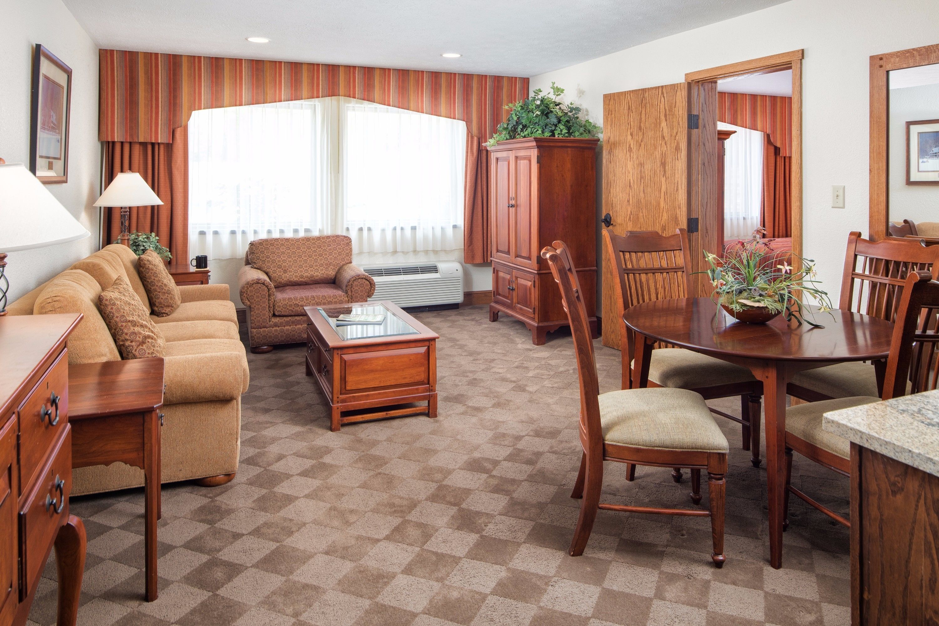 A living room with a sofa, armchair, coffee table, wooden cabinet, dining table with chairs, and a potted plant.