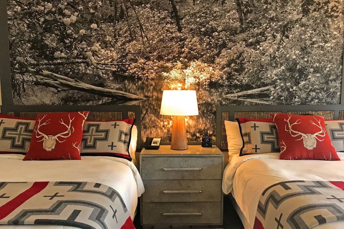 Un lit double avec une couvre-lit à motifs, deux oreillers ornés d’une croix et de têtes de cerf, une table de chevet avec une lampe, une horloge et un téléphone.