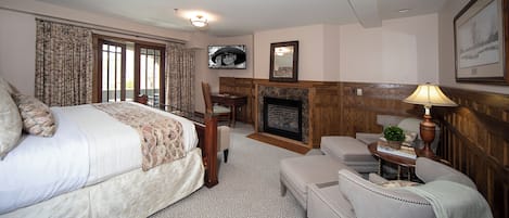 Ein Schlafzimmer mit einem Bett, einem Schreibtisch, einem Sessel, einem Kamin und einem Fernseher.