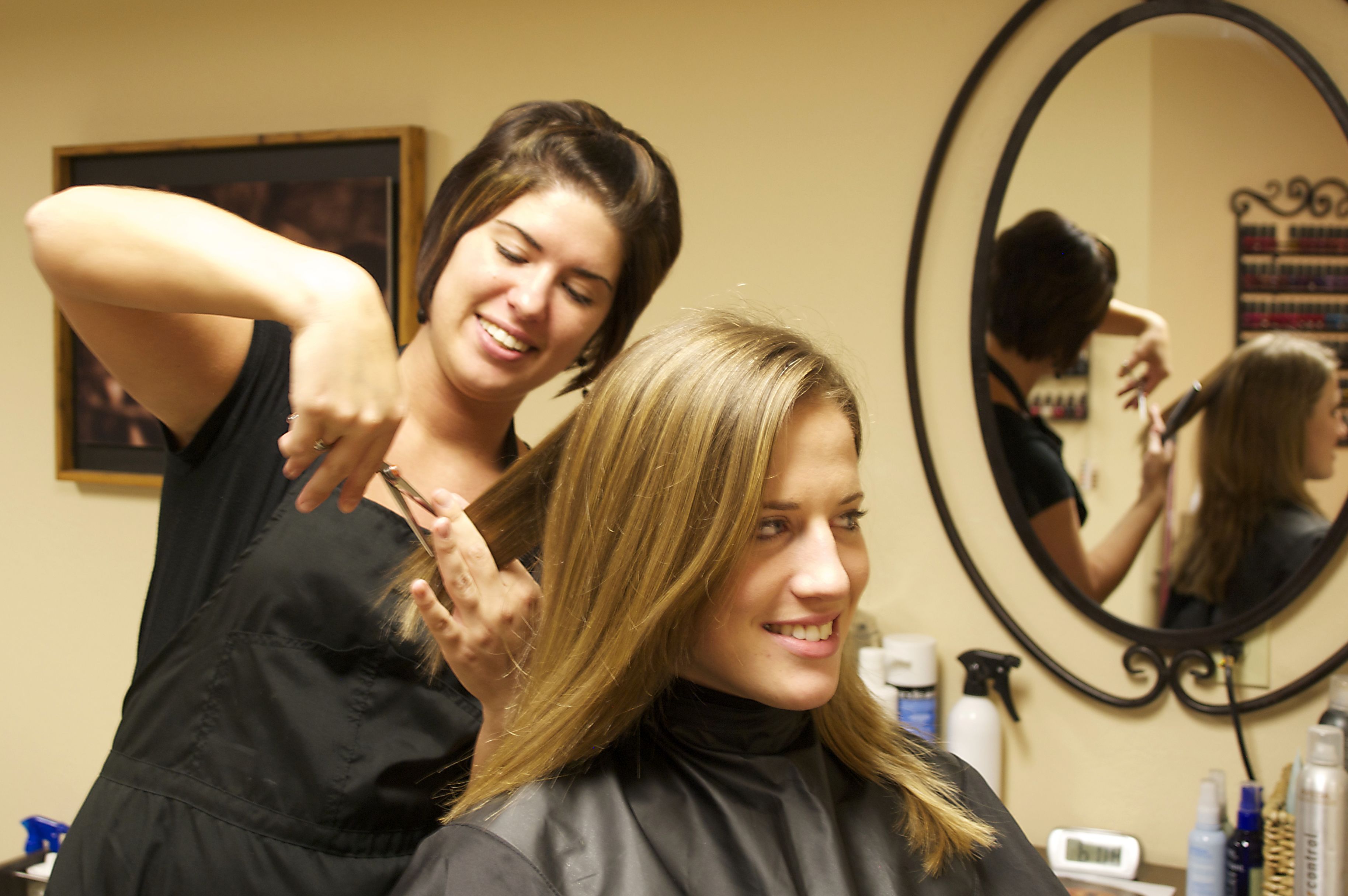 A salon interior with a mirror, hair products, and a client receiving a haircut.