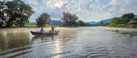 A calm river with a boat carrying two people, surrounded by lush greenery and a clear sky.