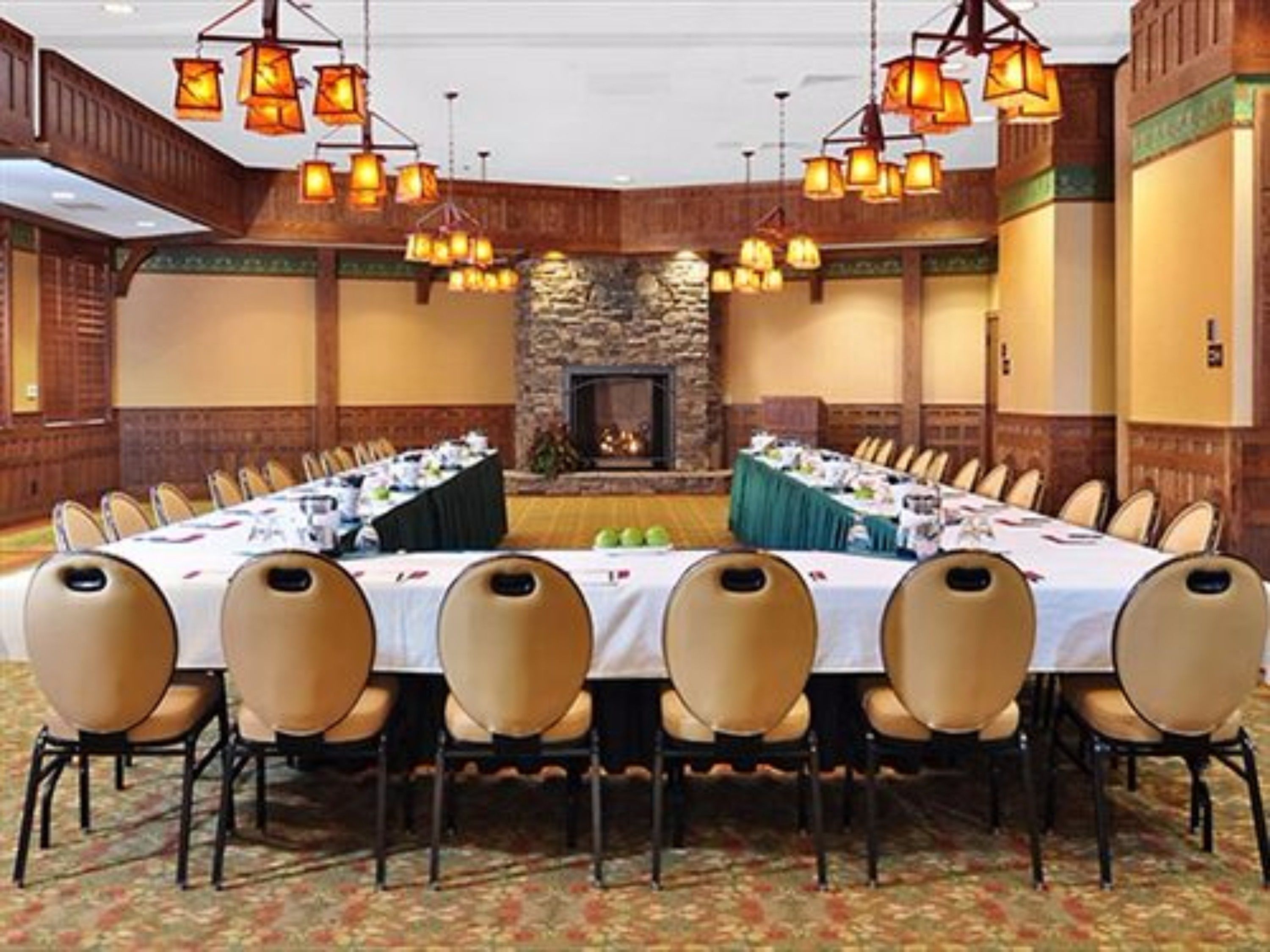 A conference room with a long table set for a meeting, surrounded by chairs, with a stone fireplace and hanging lanterns.