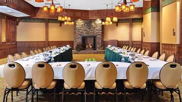 A conference room with a long table set for a meeting, surrounded by chairs, with a stone fireplace and hanging lanterns.