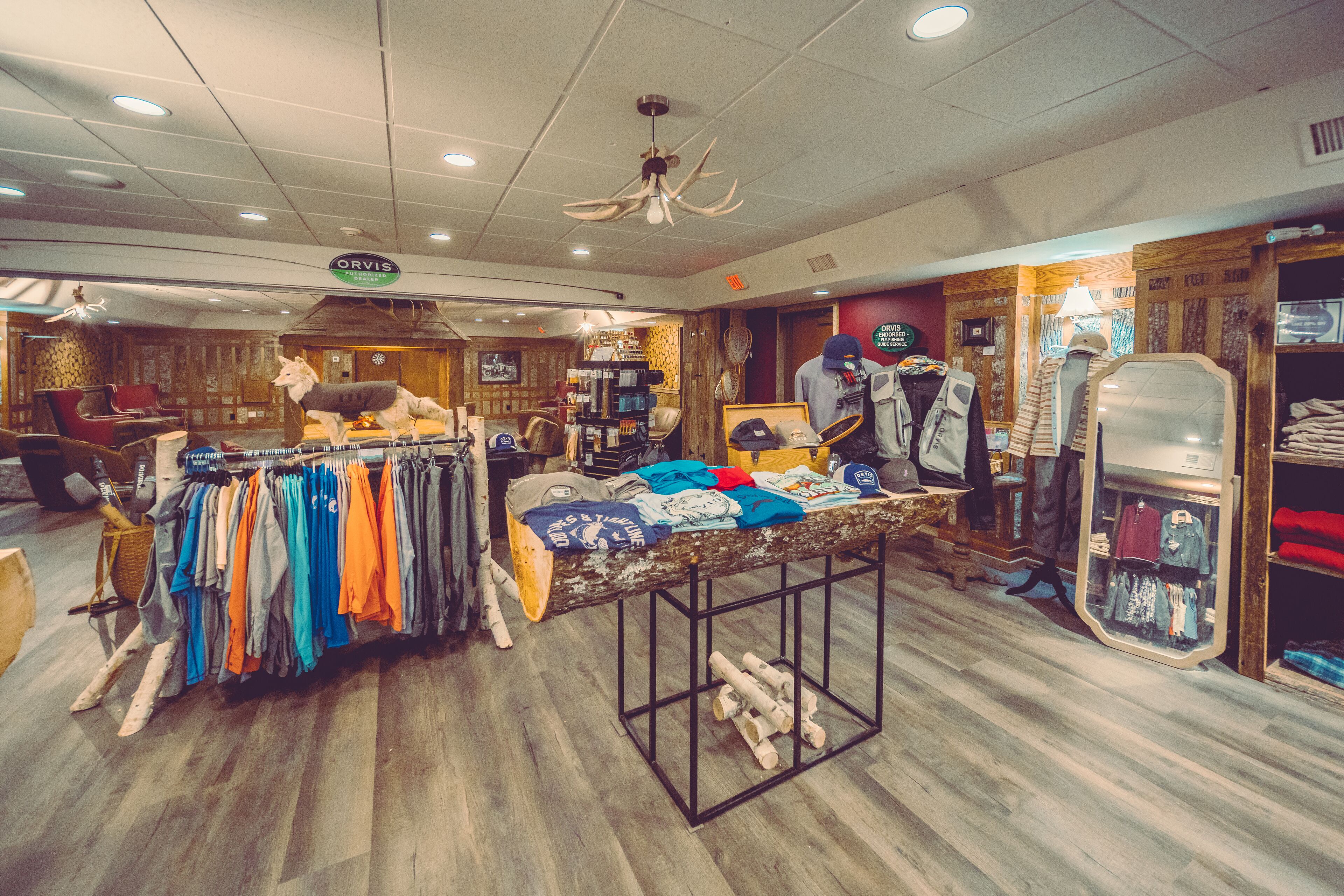 A clothing store with a wooden interior, a central display table, and a mirror reflecting the clothing.