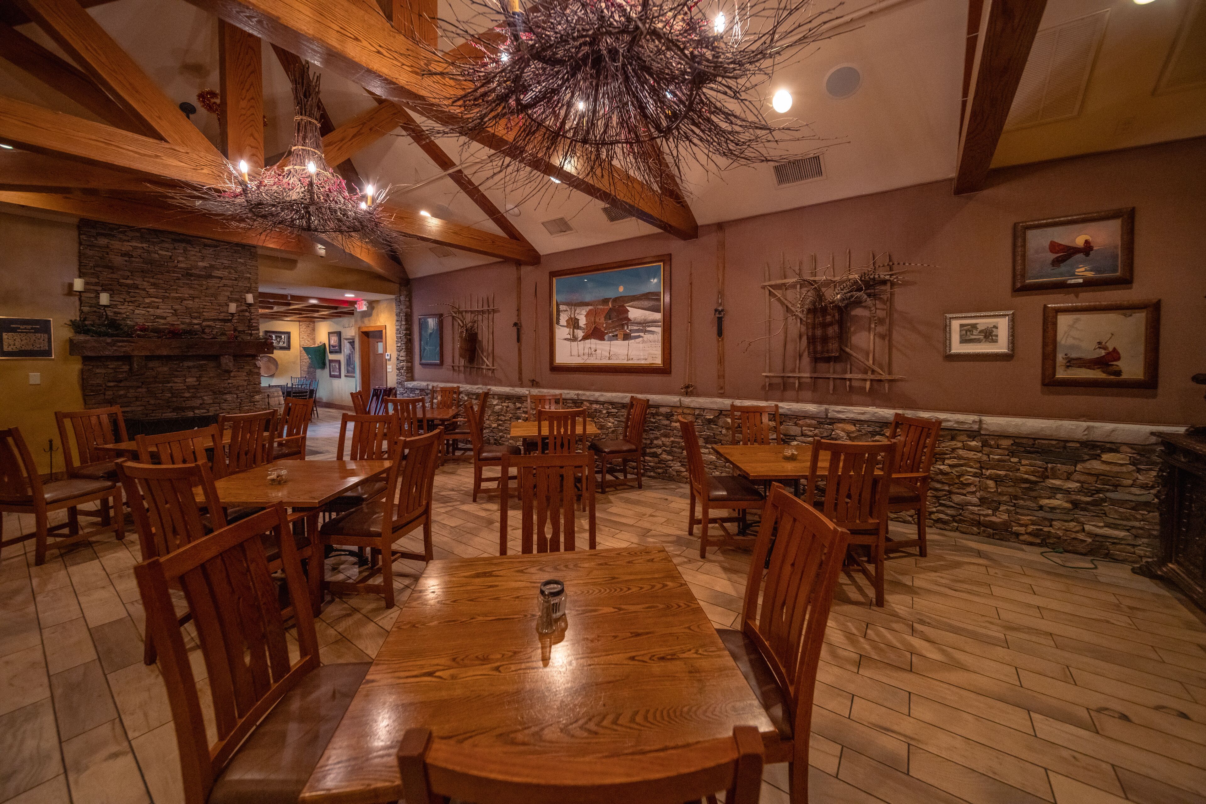 A restaurant with wooden tables and chairs, stone walls, and a rustic chandelier.
