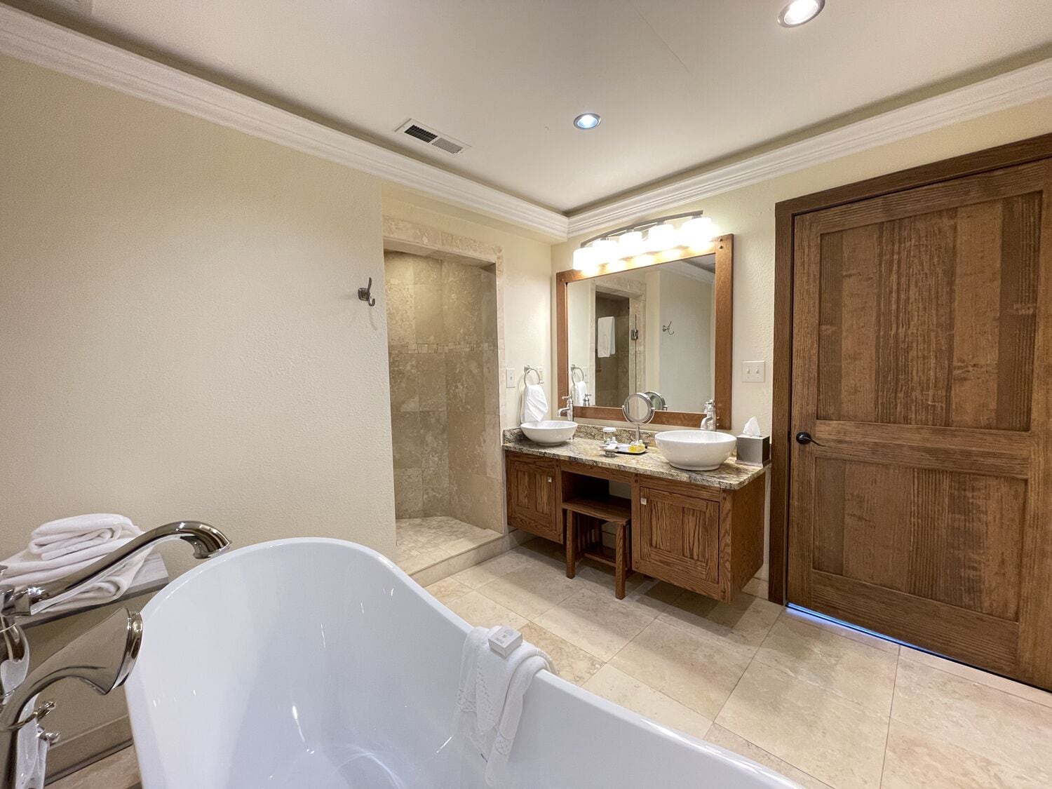 A bathroom with a freestanding bathtub, a double vanity with a large mirror, and a wooden door.