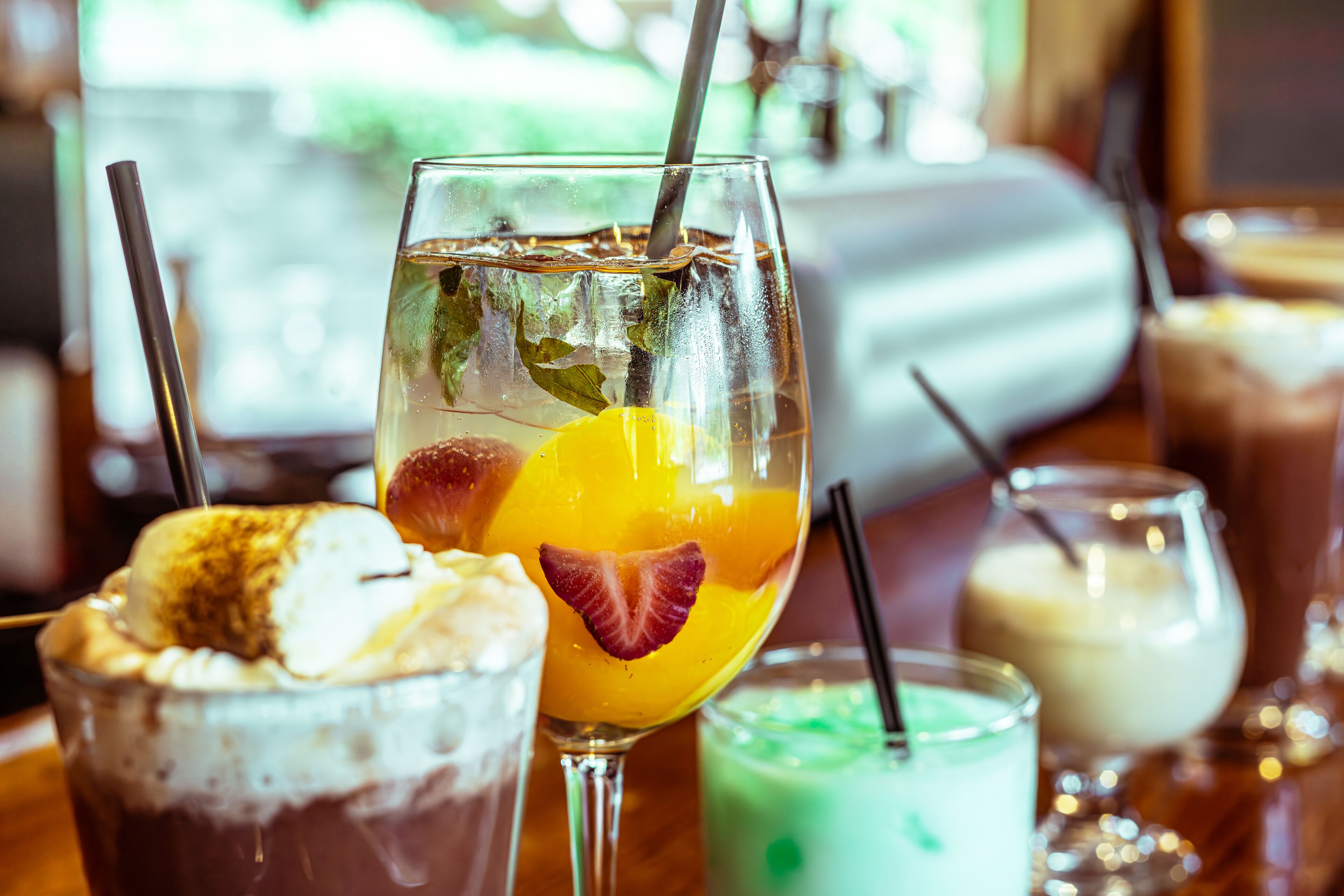 A variety of beverages in glasses, including a drink with a strawberry and a drink with a green color.