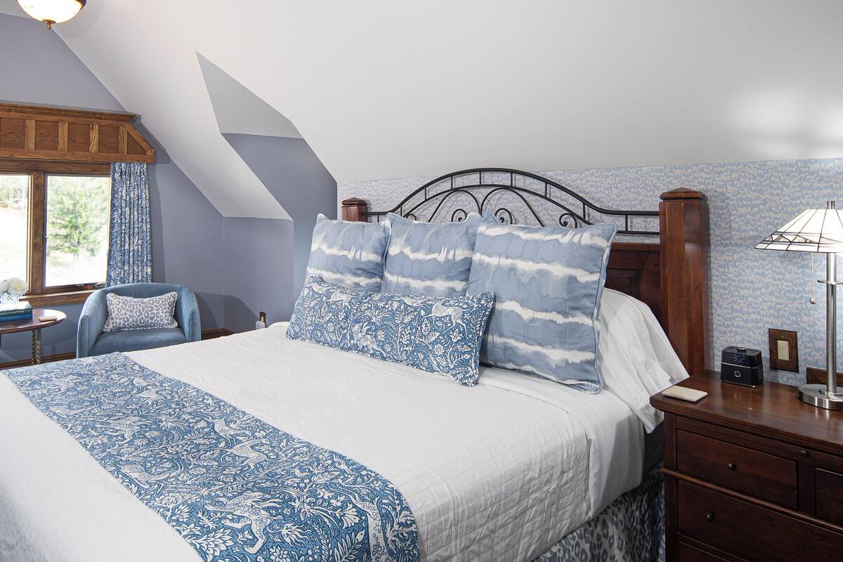 Une chambre avec un grand lit, un bureau, une chaise et une fenêtre avec des rideaux.