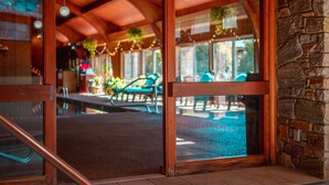 A wooden-framed glass door leading to an outdoor patio area with a pool, stone walls, and hanging plants. - Chetola Resort (Blowing Rock)