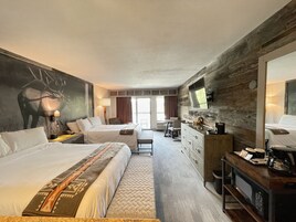 A hotel room with two beds, a desk, a dresser, a mirror, and a large window.