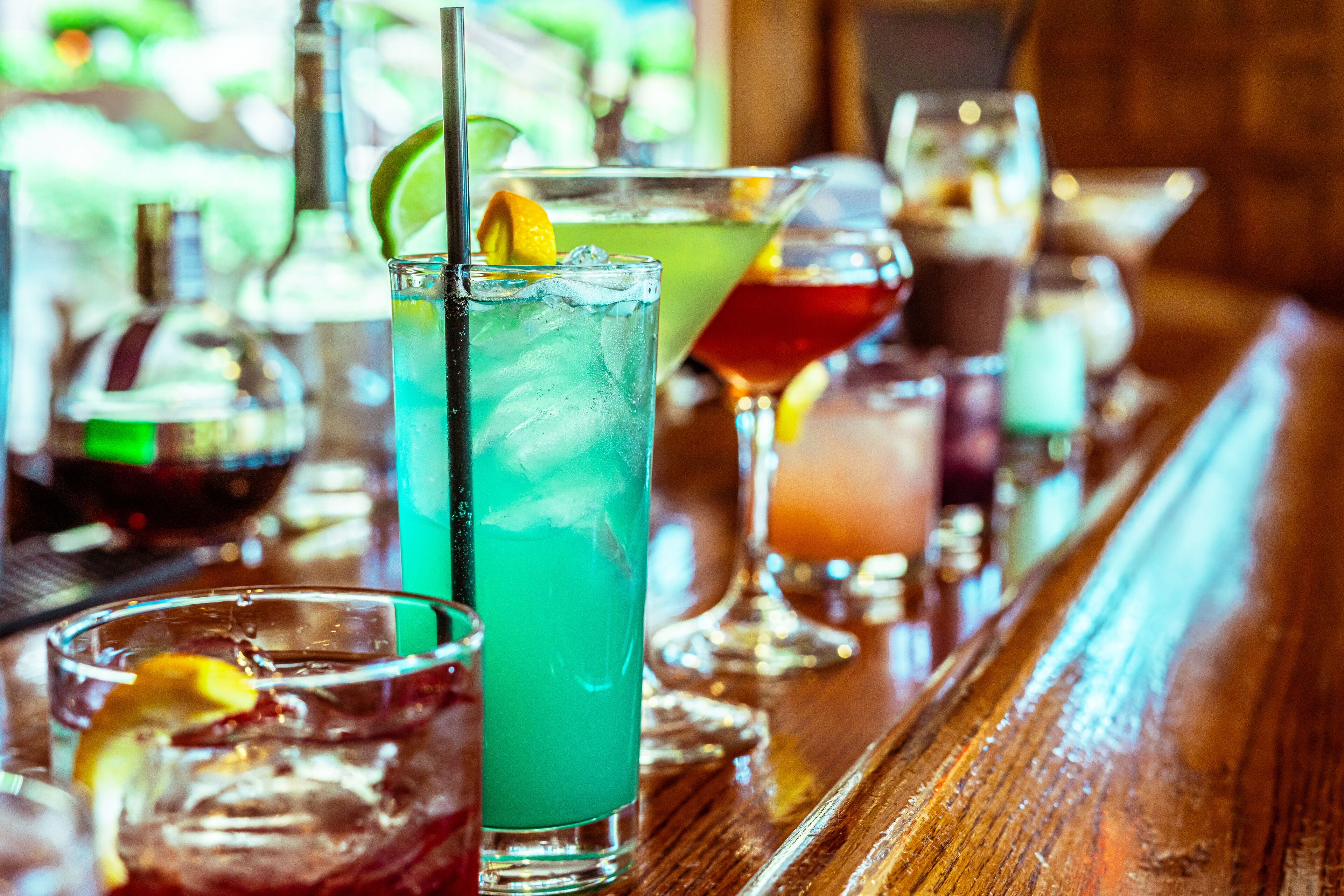 Un bar con diversas bebidas, incluyendo un vaso alto con una rodaja de lima y un trago verde.