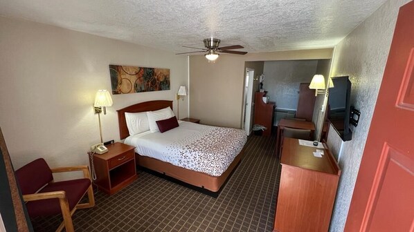 A hotel room with a bed, a desk, a chair, a telephone, a lamp, and a ceiling fan.