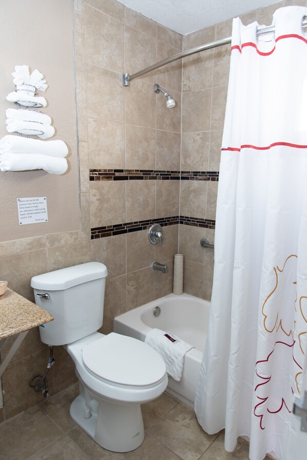 A bathroom with a toilet, bathtub, shower, and a towel rack with towels.