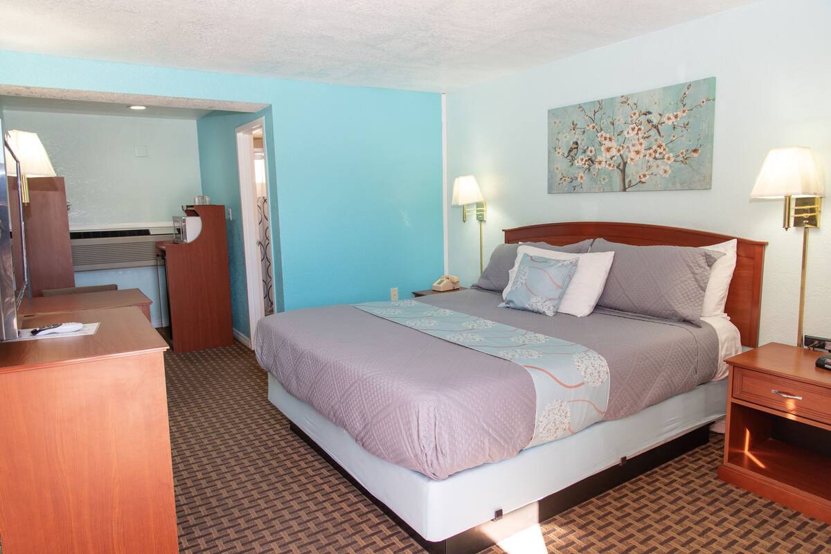 A hotel room with a large bed, bedside lamps, a desk, and a painting on the wall.
