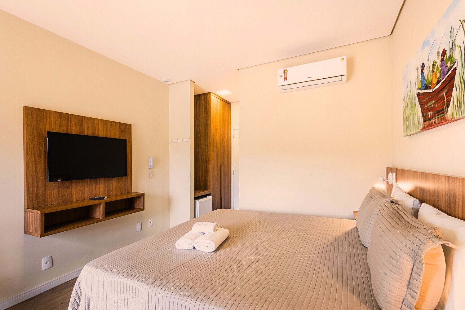 Habitación de hotel con una cama grande, televisor montado, armario y equipo de aire acondicionado.