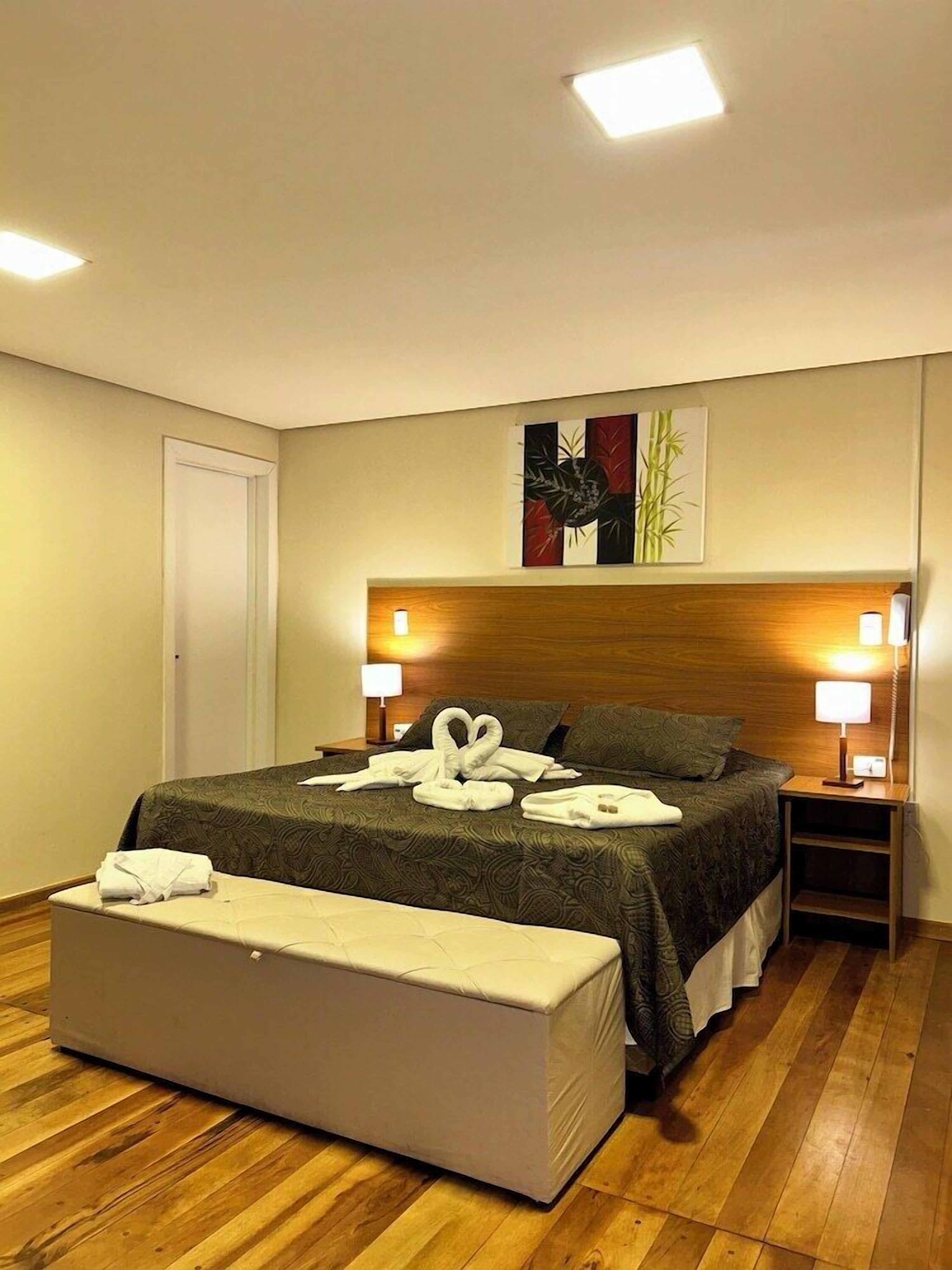Une chambre d’hôtel avec un lit, des lampes de chevet, un banc et un tableau au mur.