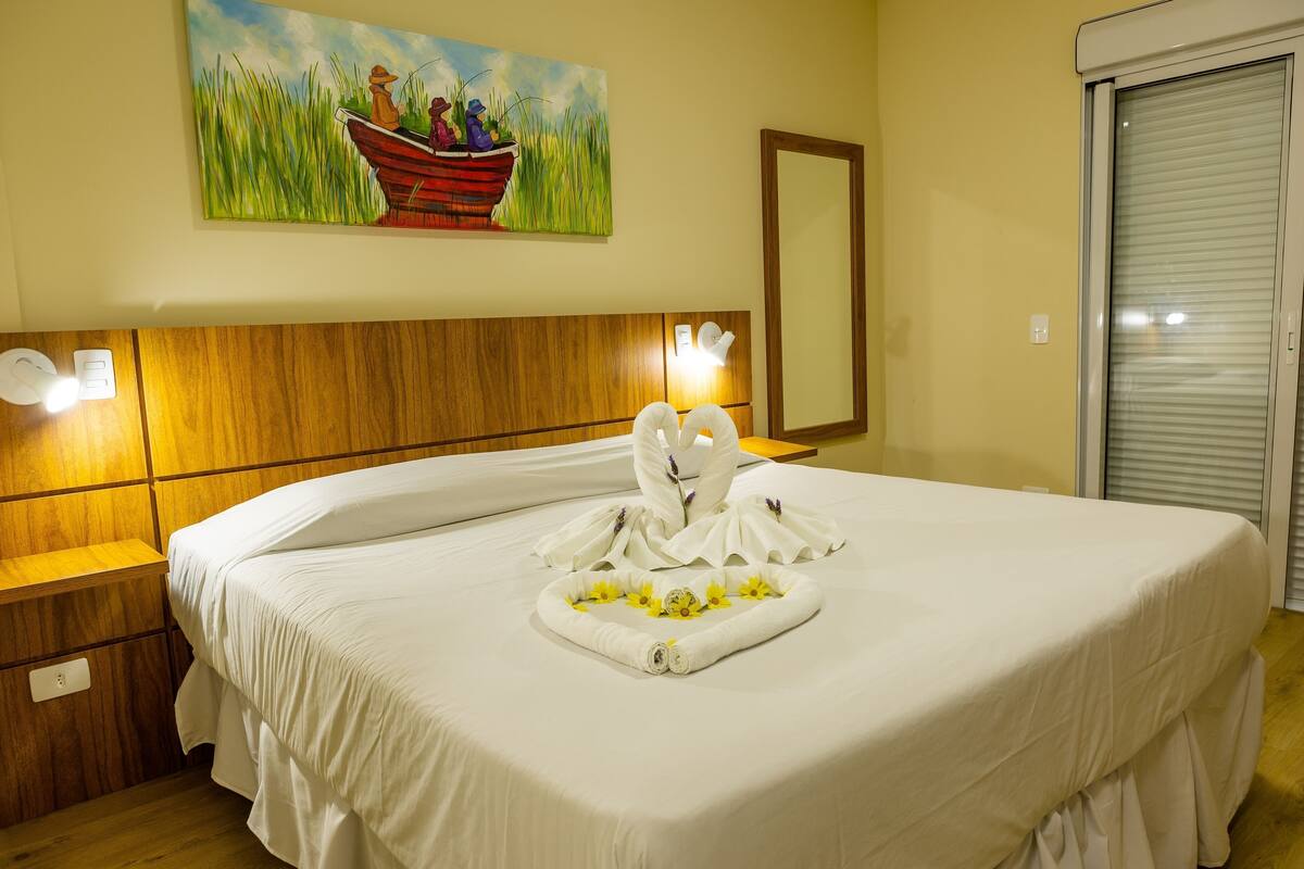A hotel room with a bed, a painting of a boat on the wall, a mirror, and a wooden headboard.