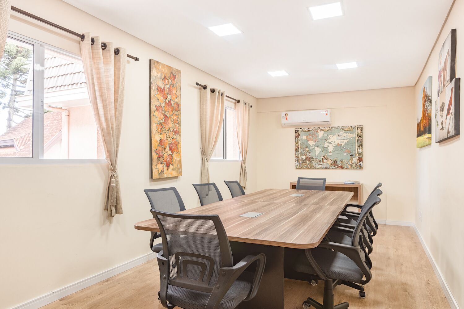 A conference room with a wooden table, six chairs, and two large paintings on the walls.