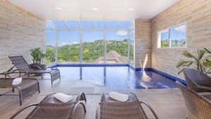 A spacious indoor swimming pool with clear views of a lush green landscape, surrounded by wicker lounge chairs and potted plants. - Kaliman Campos do Jordão (Campos do Jordão)