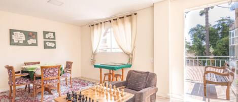 Un salón con un tablero de ajedrez, una mesa de billar y un balcón con vistas a árboles.