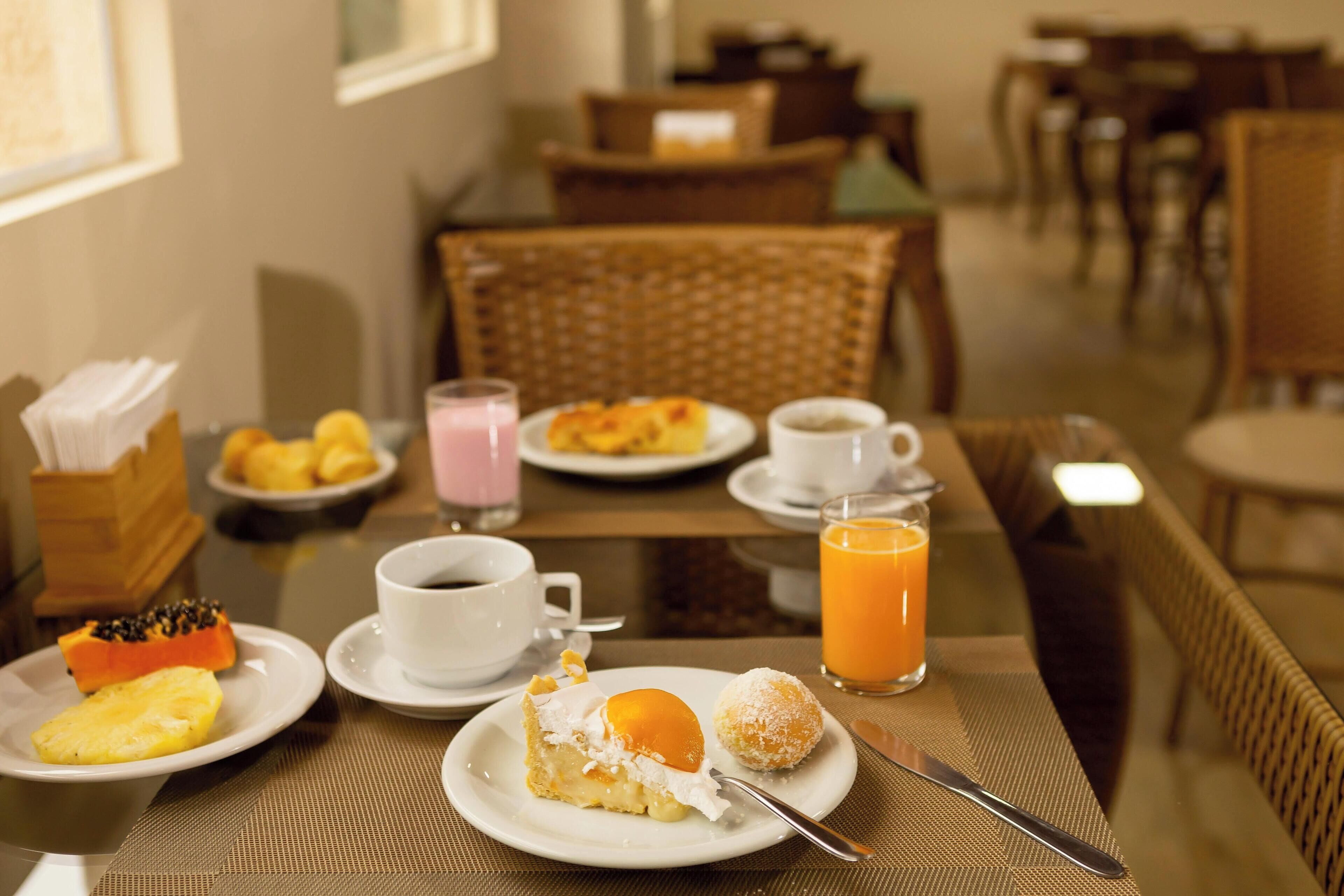 Une table mise pour le petit-déjeuner, avec des assiettes remplies de nourriture, une tasse de café et un verre de jus d’orange.