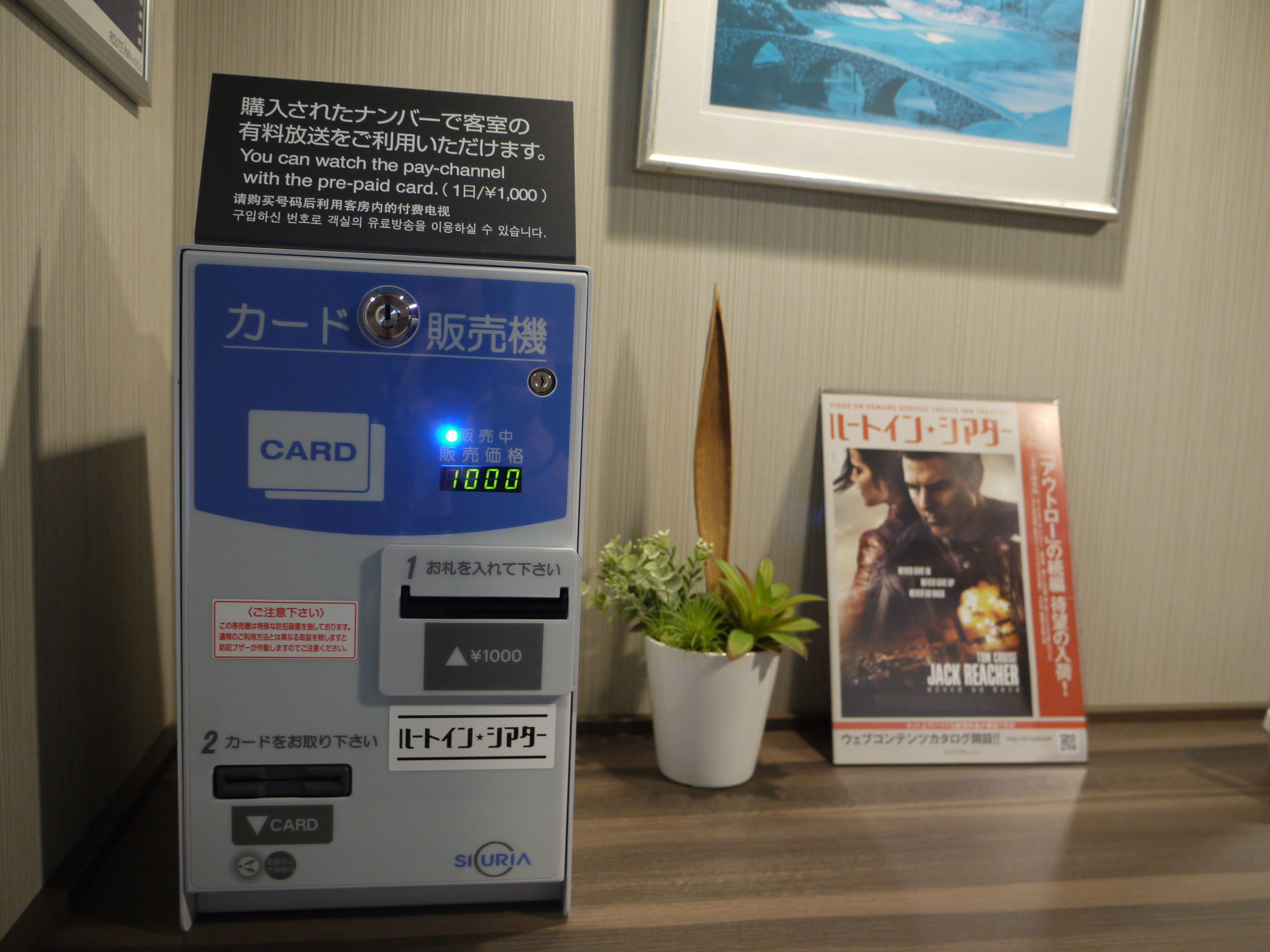 A card reader with a digital display, a potted plant, and a movie poster on a table.