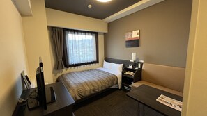 A hotel room with a bed, bedside table, lamp, and a small table with a newspaper.