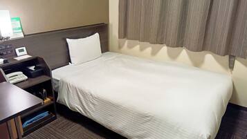 A hotel room with a single bed, a bedside table with a phone and a lamp, and a small shelf with a tissue box and a book.