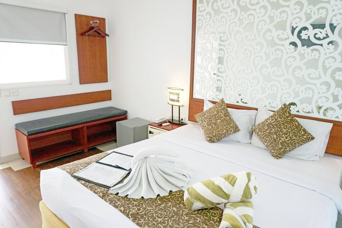 A neatly made bed with patterned pillows, a bedside lamp, a wooden bench, and a wall-mounted hanger.